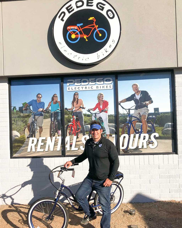 Man standing with an electric bike outside of a Pedego store.|