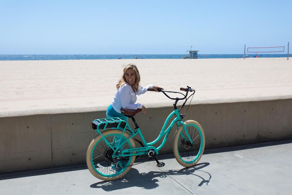 Denise Austin standing with her Pedego bike on the beach.