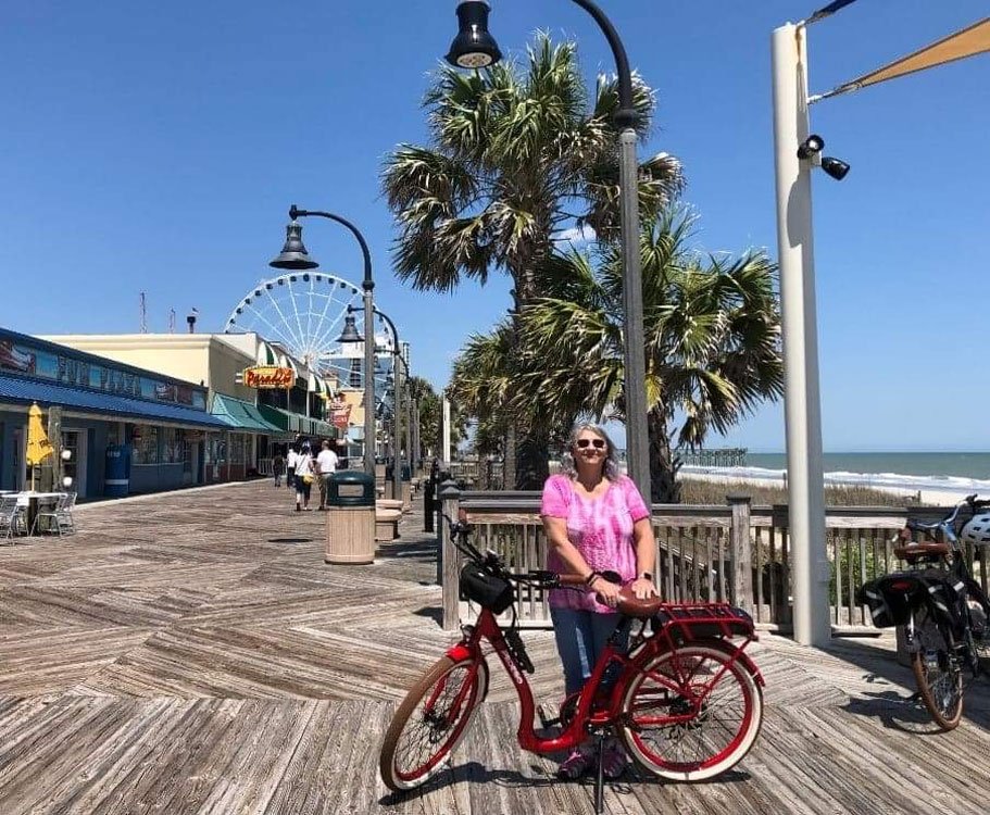 Pedego customer Linda Snyder standing with her bike on a boardwalk.